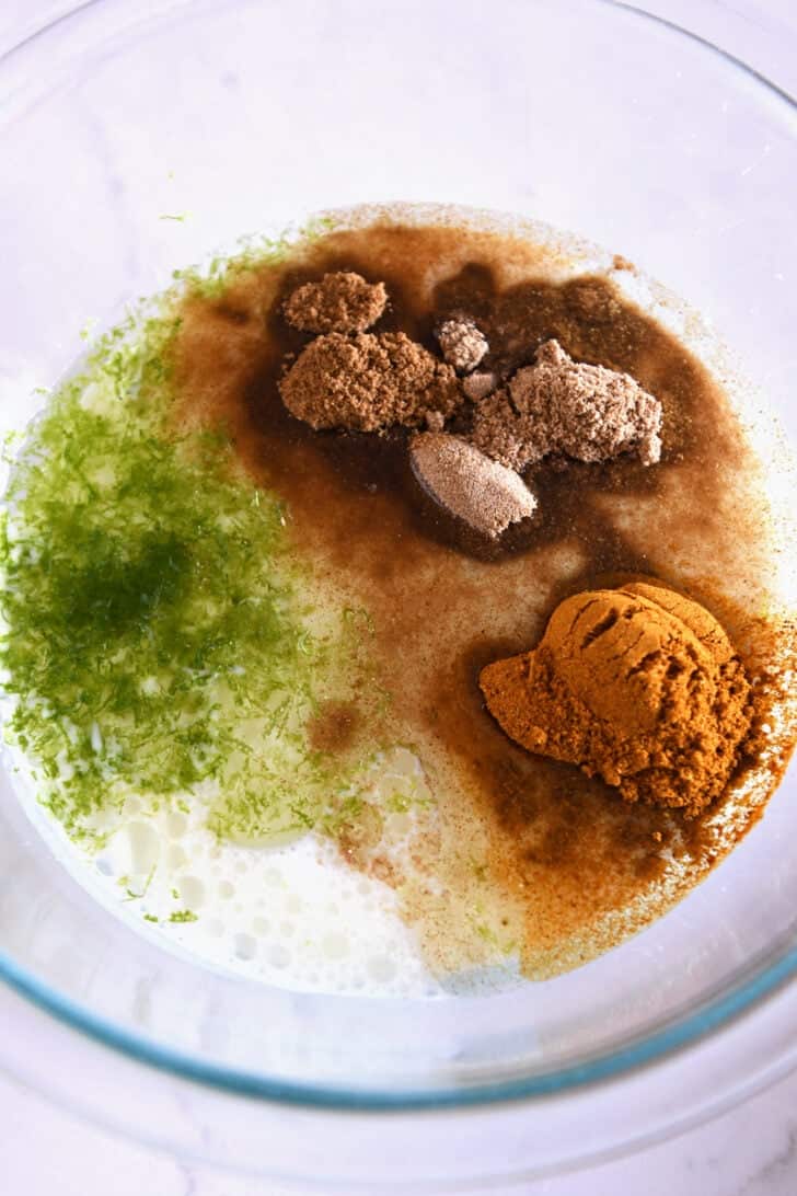 Glass bowl with coconut milk, lime zest, curry powder, coriander and cumin.