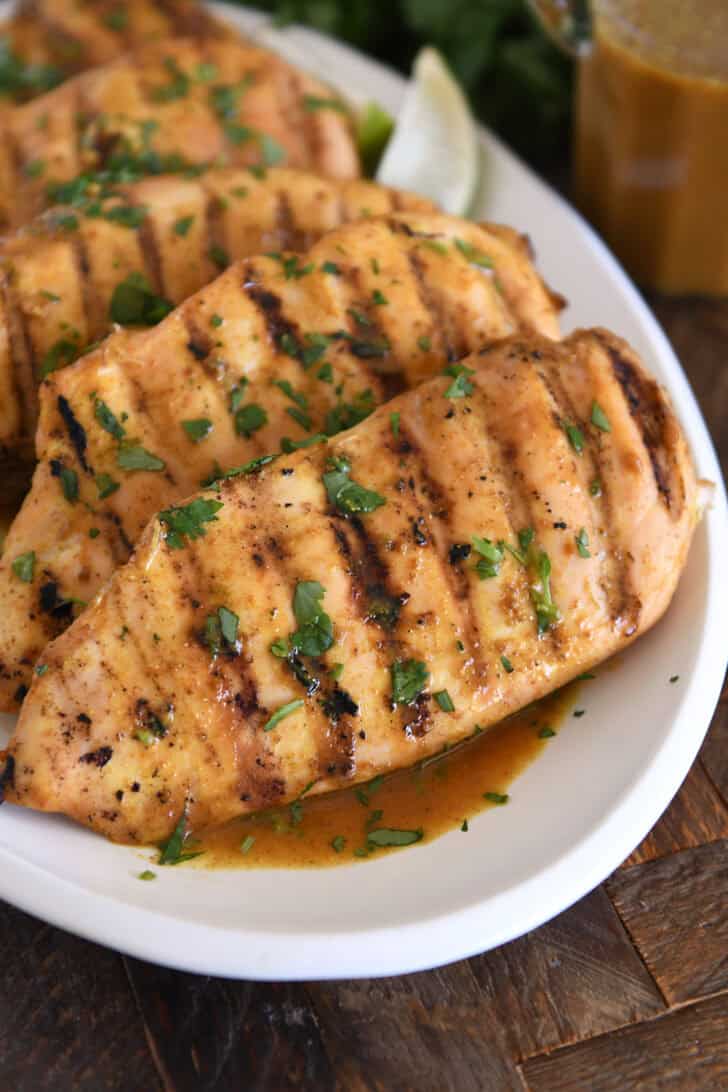 Grilled chicken breasts with cilantro and sauce on white tray.
