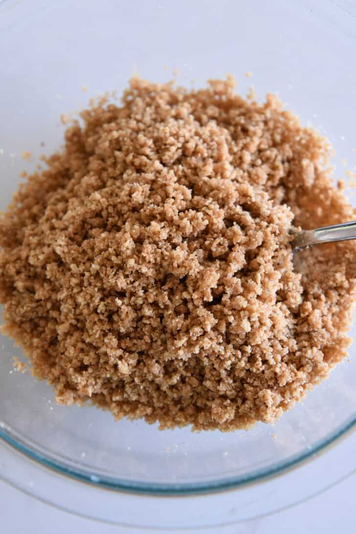 Top down view of buttered graham cracker crumbs in glass bowl.