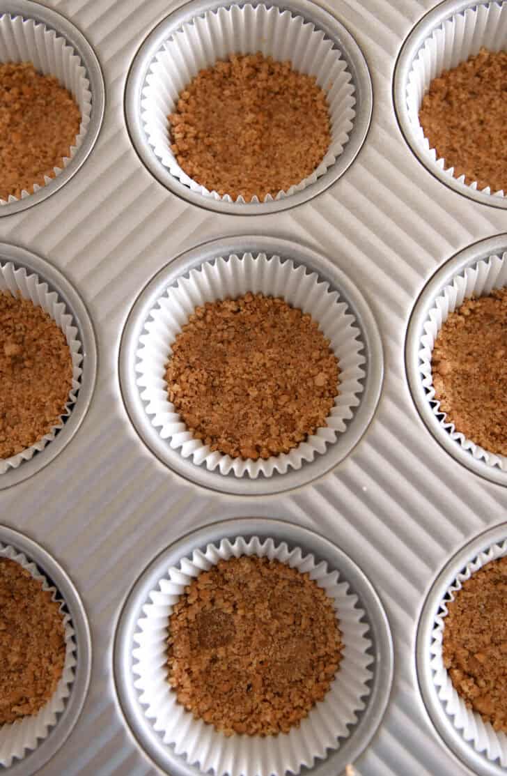 Top down view of graham cracker crust pressed into lined muffin tin.