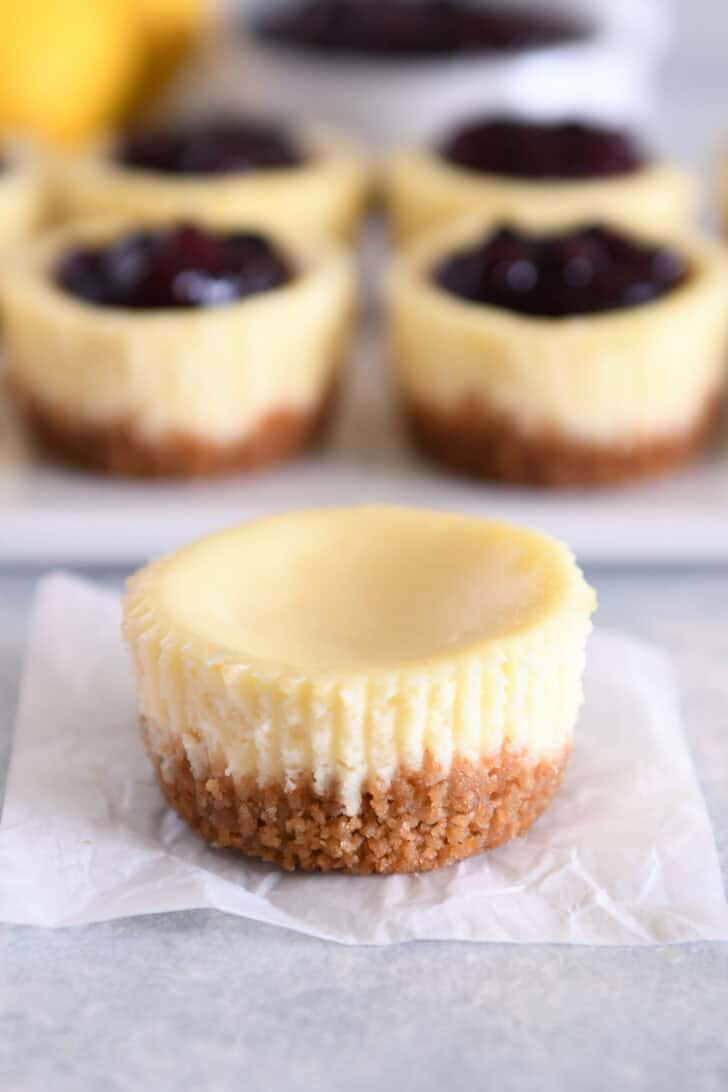 One untopped plain mini cheesecake on piece of square white parchment paper.