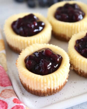 Four mini cheesecakes with huckleberry topping on white tray.