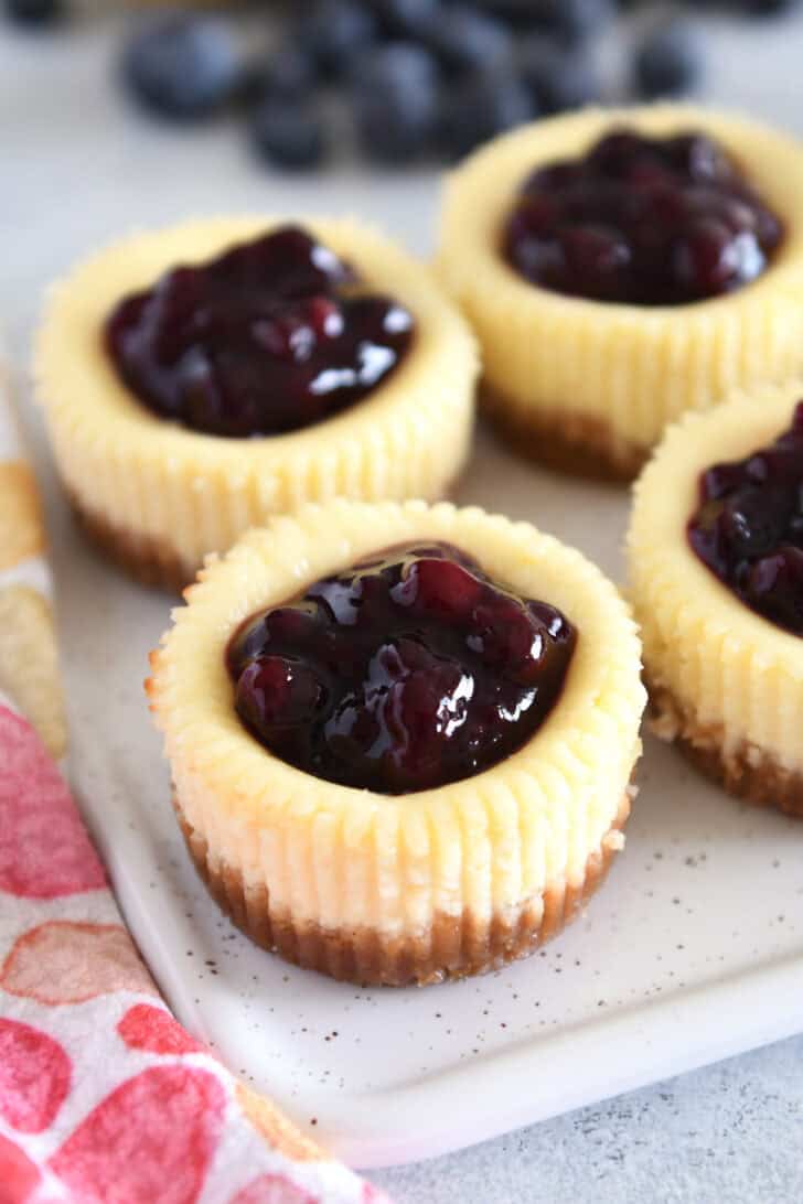 Four mini cheesecakes with huckleberry topping on white tray.