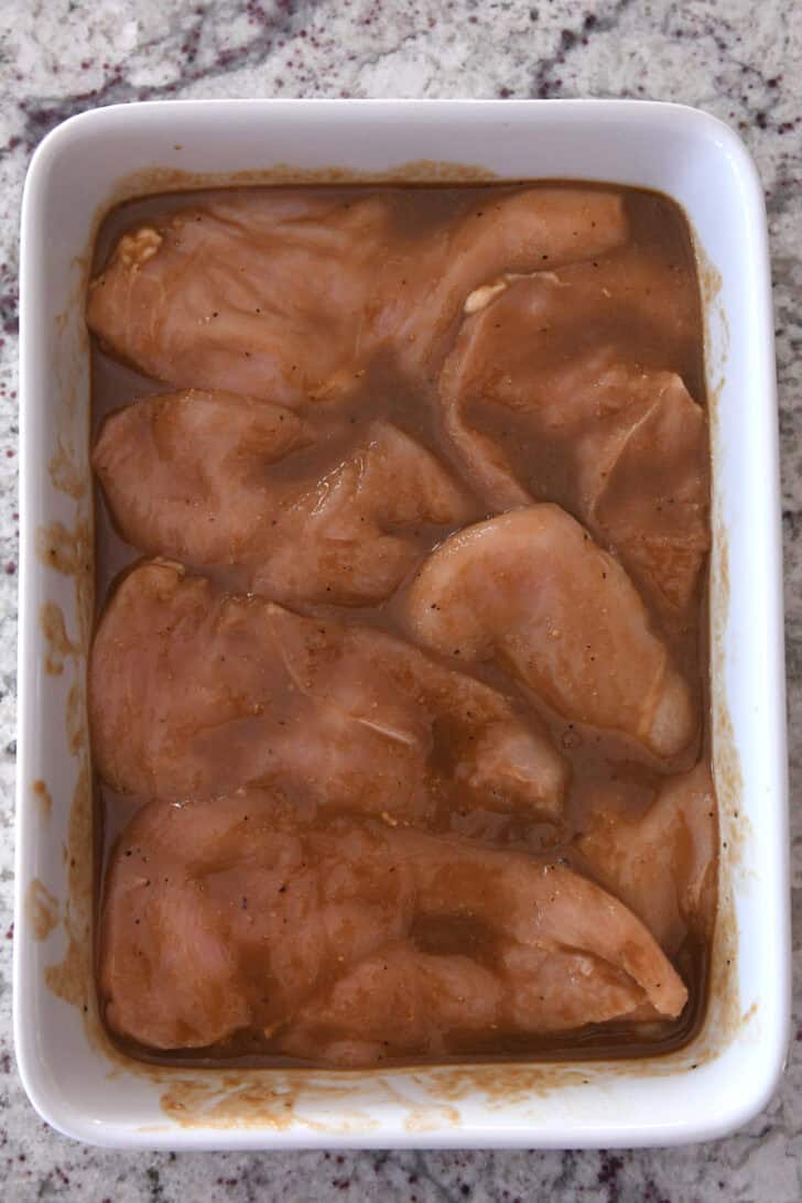 White pan with chicken breasts and marinade.
