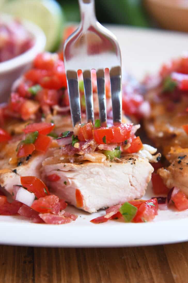 Fork spearing bite of cooked chicken, bacon, tomatoes, jalapenos and cheese.