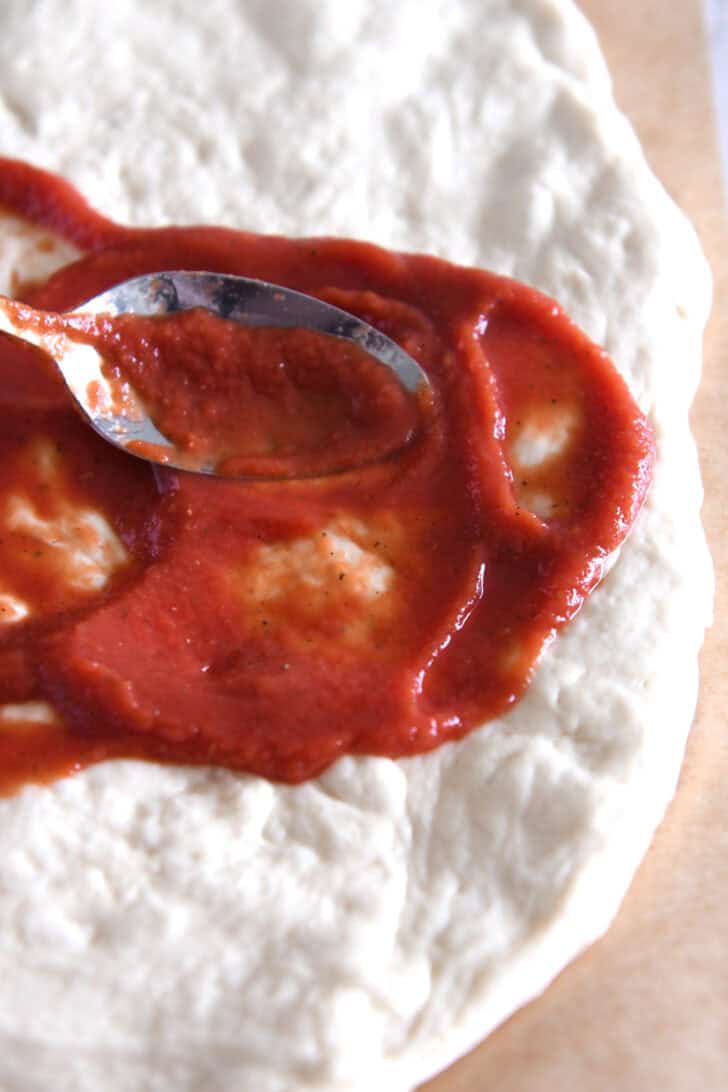 Spreading pizza sauce on pizza dough.