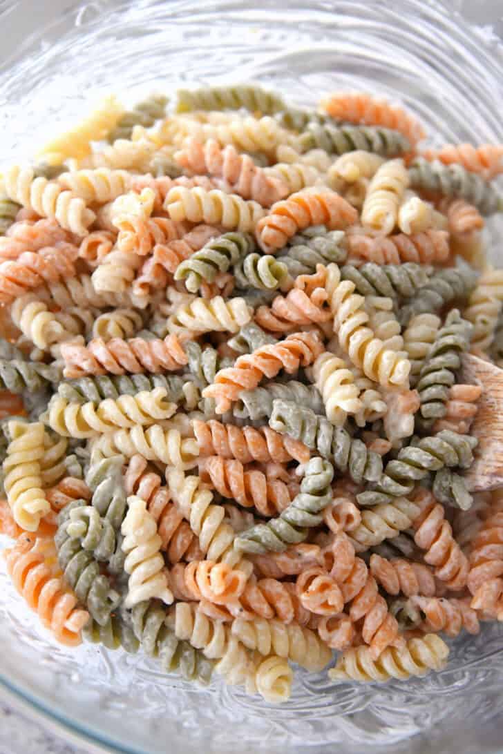 Top down view of caesar dressing-coated tri-color pasta in glass bowl.