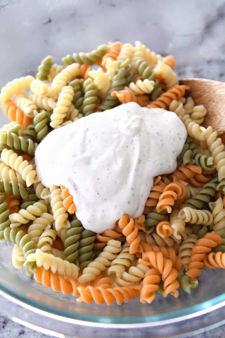 Dollop of caesar salad dressing on cooked pasta in glass bowl.