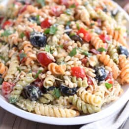 Pasta salad on oval white tray with olives, tomatoes, parmesan cheese and fresh basil.