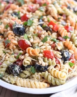 Pasta salad on oval white tray with olives, tomatoes, parmesan cheese and fresh basil.