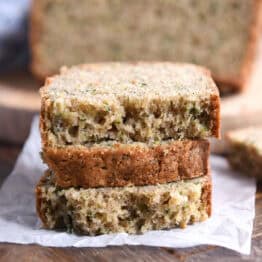 Three half slices of zucchini bread stacked on piece of parchment paper.