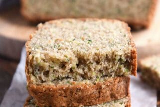 Three half slices of zucchini bread loaf stacked on white parchment paper.