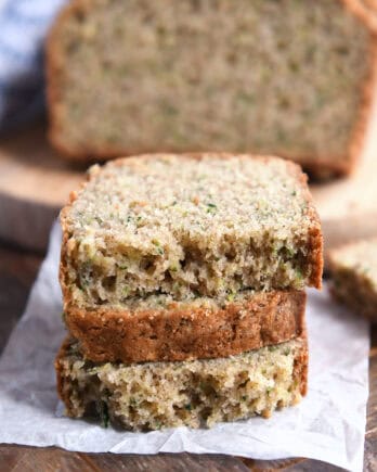 Three half slices of zucchini bread loaf stacked on white parchment paper.