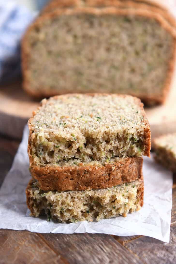 Three half slices of zucchini bread loaf stacked on white parchment paper.