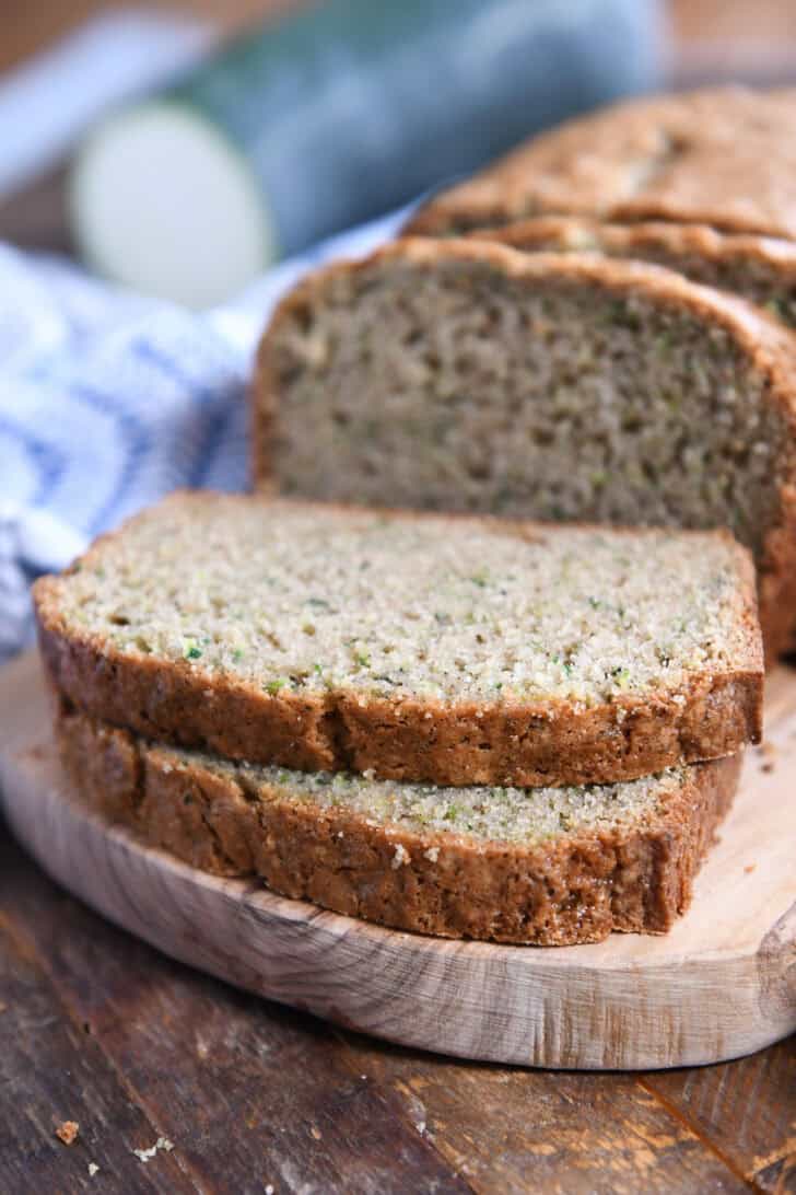 Two slices cut from loaf of zucchini bread on wood cutting board.