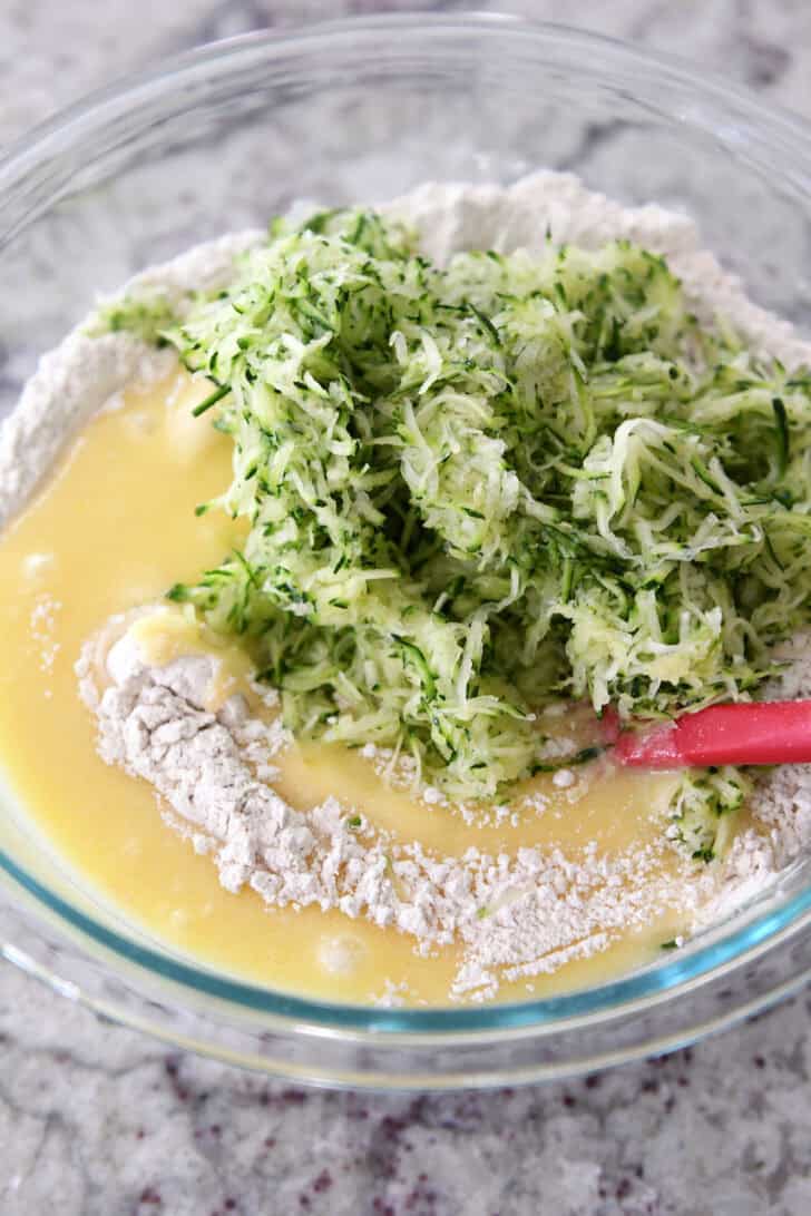 Glass bowl with flour, egg mixture and shredded zucchini.