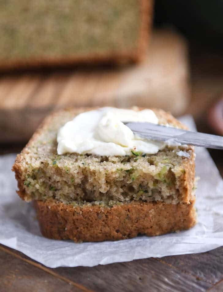 Spreading cream cheese on top of half slice of zucchini bread.