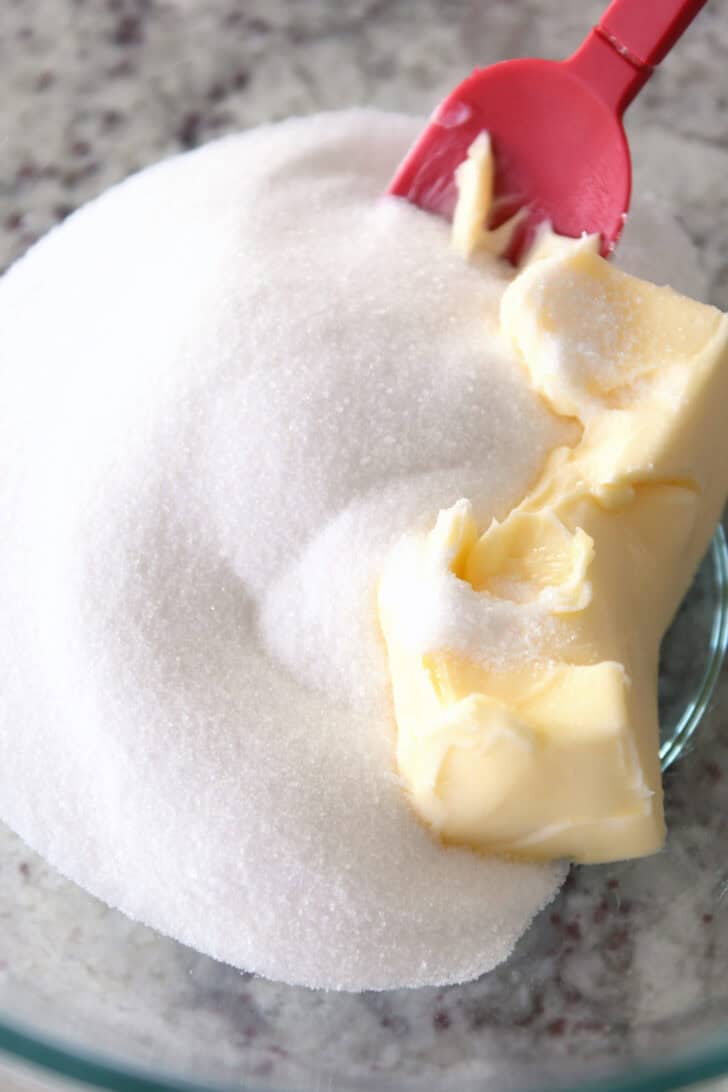 Top down view of a glass bowl with granulated sugar and soft butter.