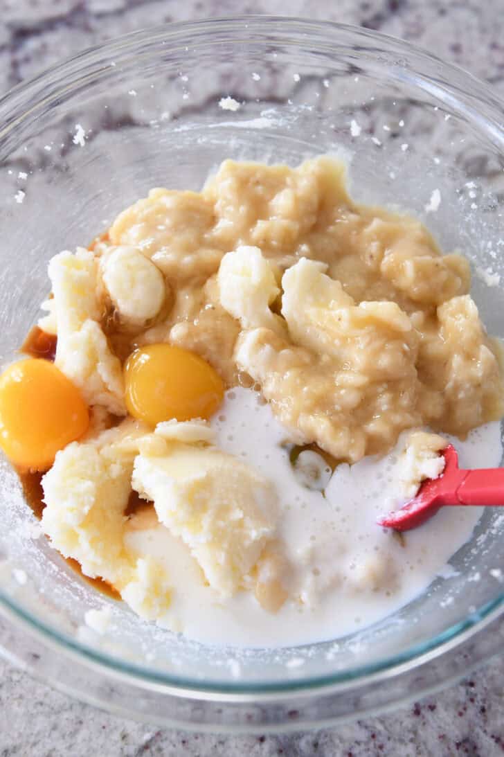Top down view of ingredients for banana bread in a glass bowl.