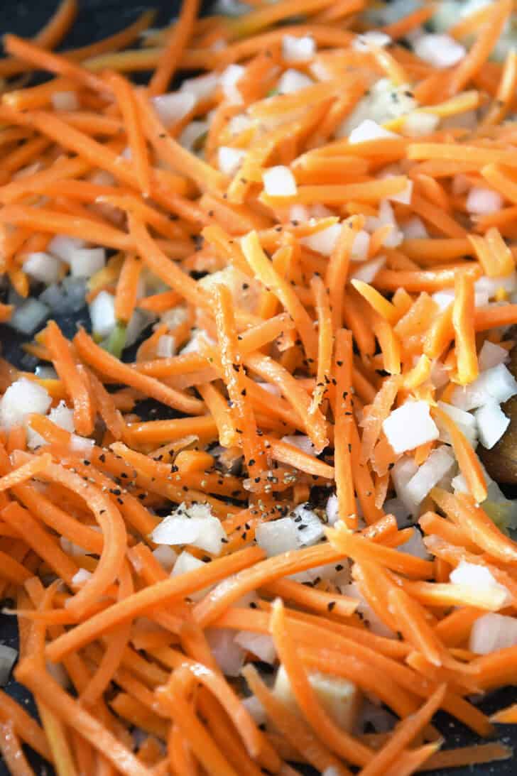 Top down view of matchstick carrots and onion being cooked in a skillet.