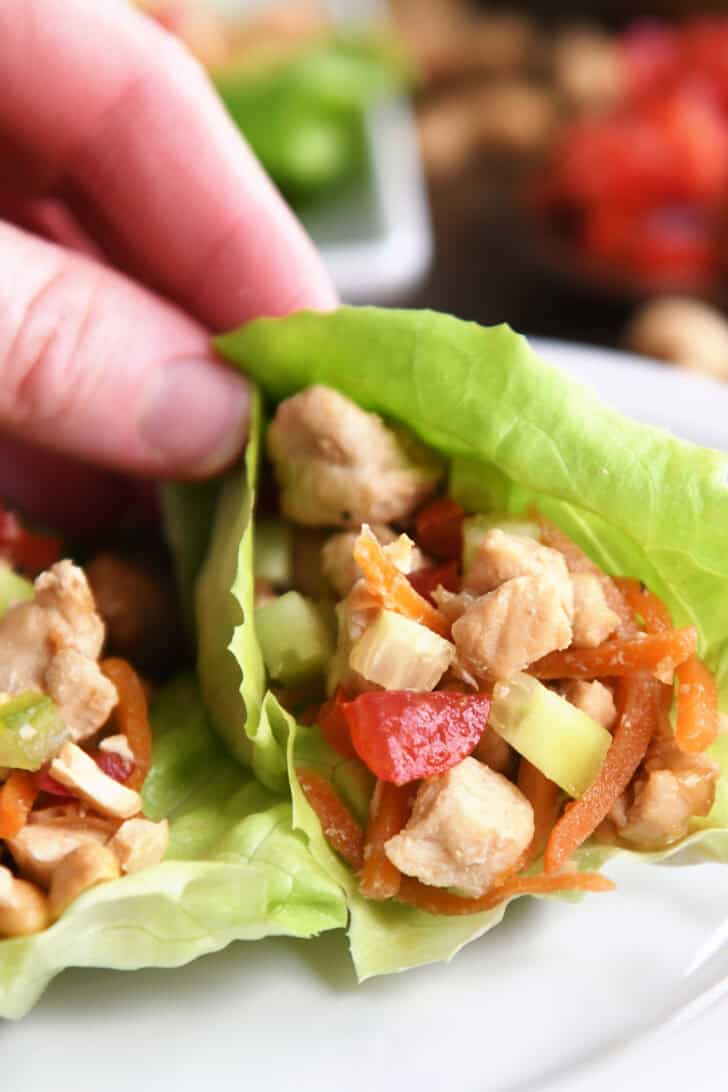 A hand holding a lettuce wrap full of a chicken vegetable mixture.