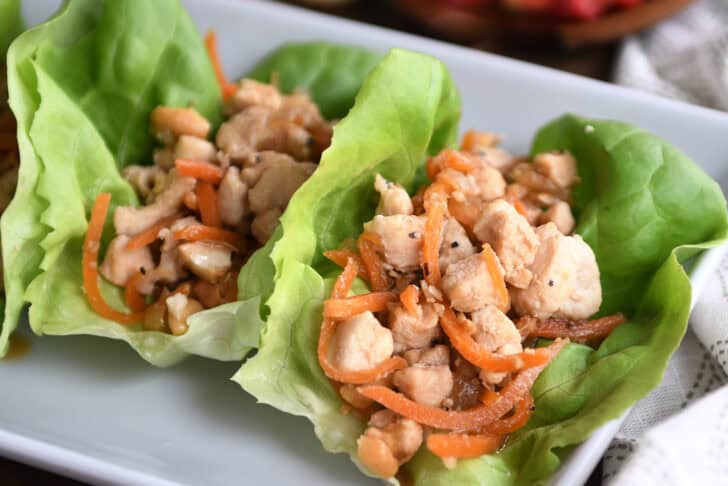 Top down view of a chicken and carrot lettuce wrap on a white platter.
