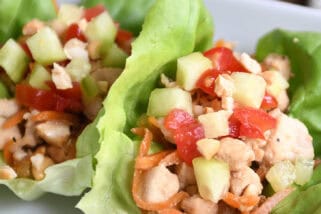 Top down view of lettuce leaves full of a chicken vegetable mixture on a white plate.
