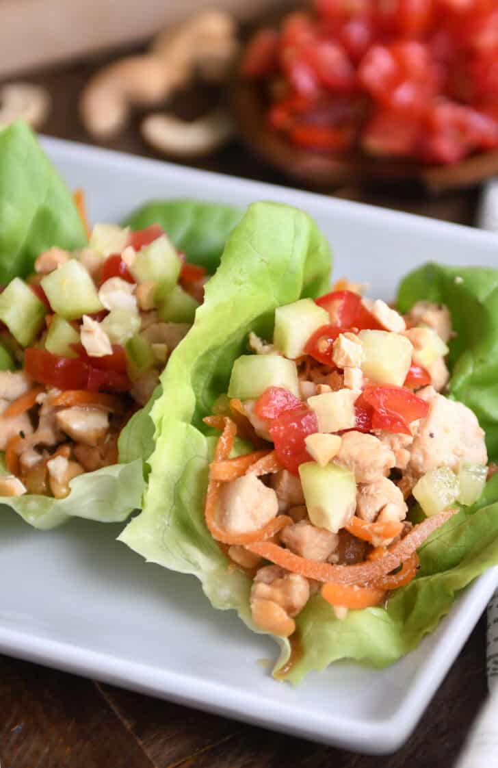Top down view of lettuce leaves full of a chicken vegetable mixture on a white plate.