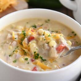 A white bowl with a spoon taking a bite of chicken corn chowder out of the bowl.