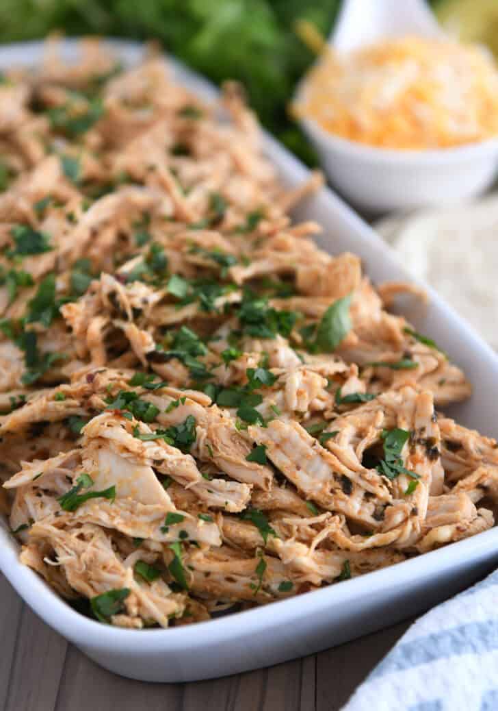 A white dish filled with shredded cooked and seasoned chicken sprinkled with green herbs.