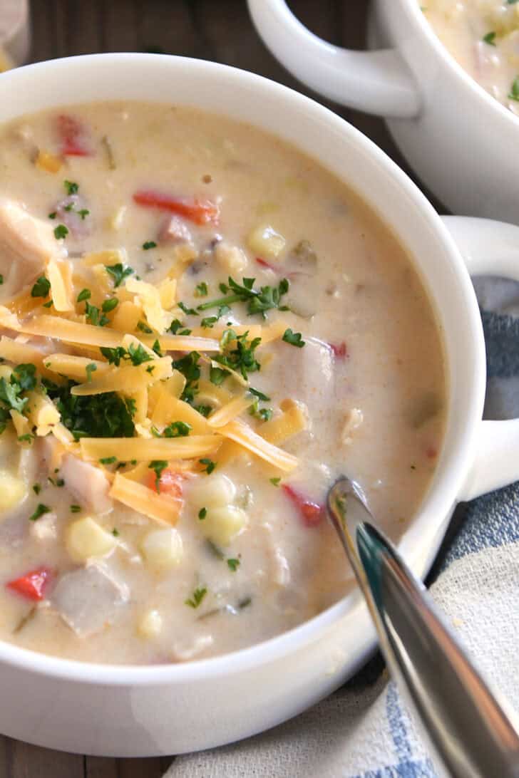 Top down view of a white bowl filled with chicken corn chowder topped with shredded cheese and parsley.