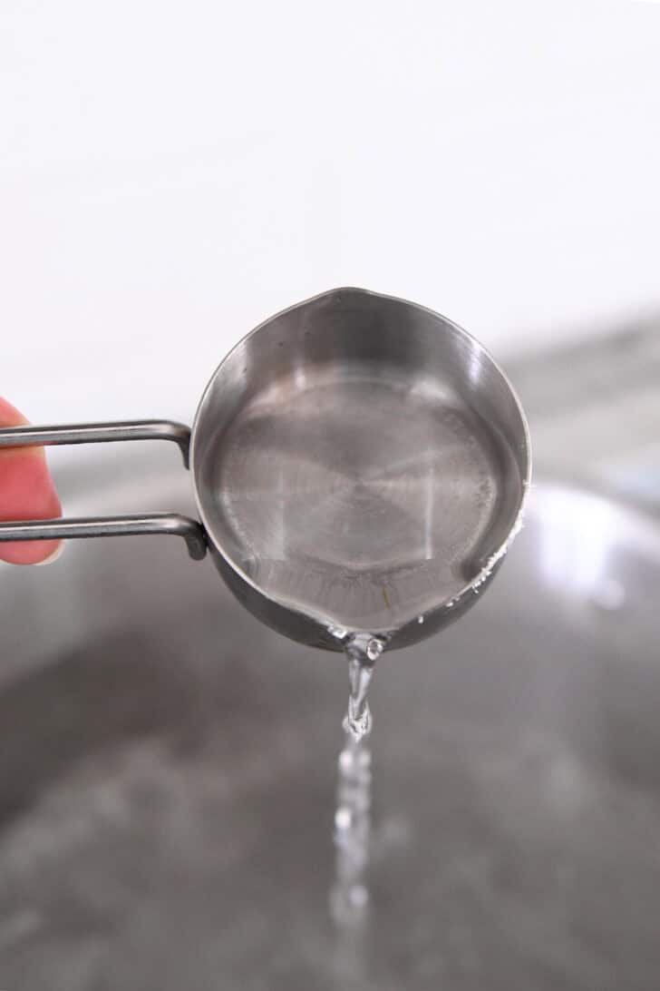 A metal measuring cup pouring vinegar into a pot of water.