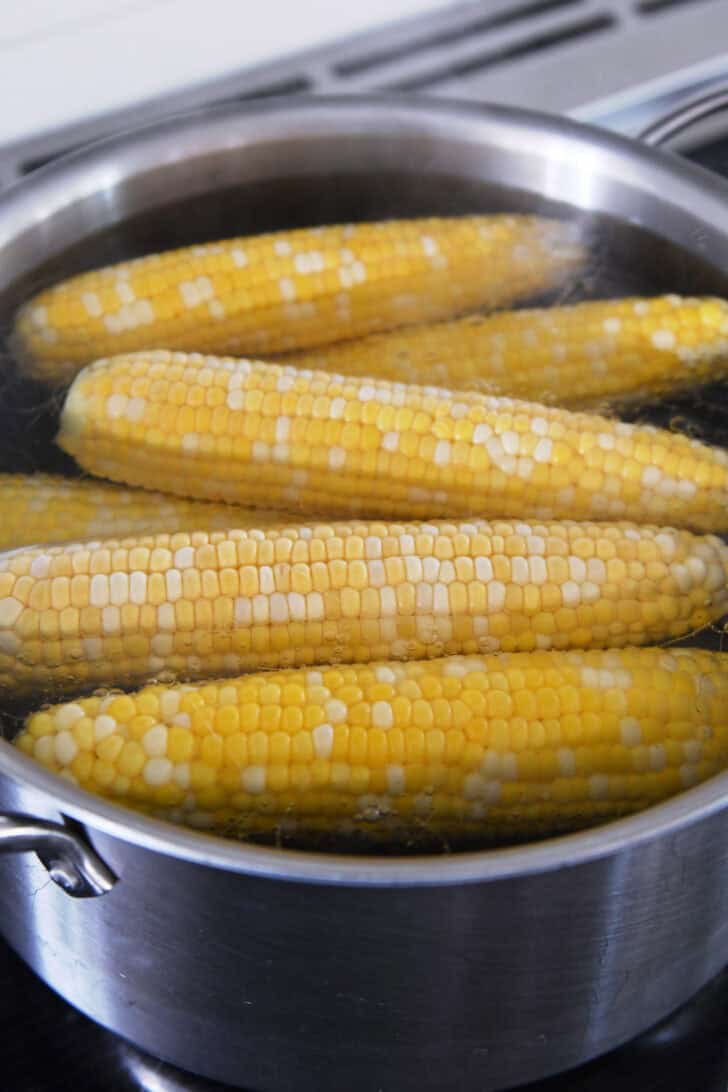 A metal pot with fresh corn on the cob cooking in it.