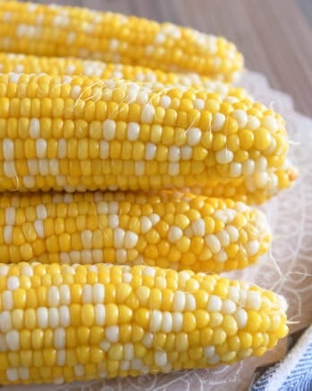 Fresh corn on the cob stacked on top of each other on a decorative platter.