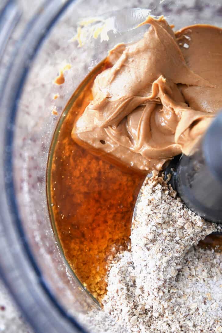 Top down view of peanut butter, honey, and oats in the bottom of a food processor.