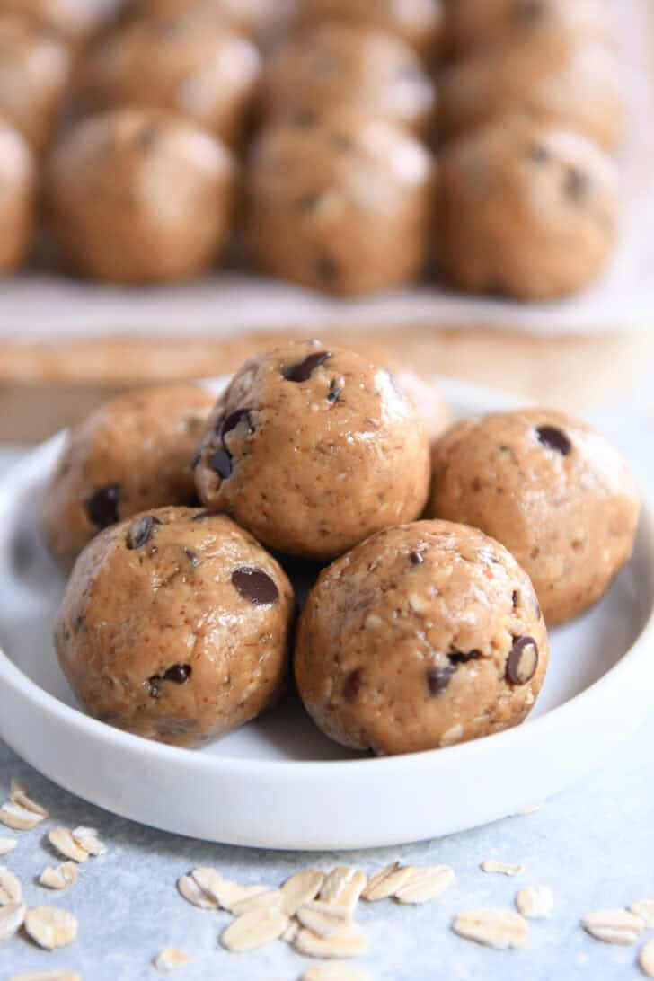 Peanut butter chocolate chip balls staked on top of each other in a small round white dish. More peanut butter balls are in the background.