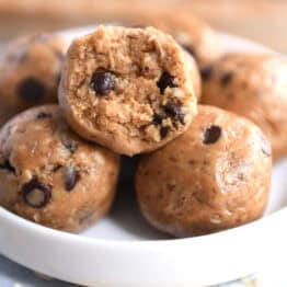 Soft peanut butter chocolate chip balls in a small white dish. The top ball has a bite taken out.