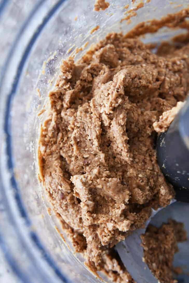 Top down view of a peanut butter oat mixture in the bottom of a food processor.