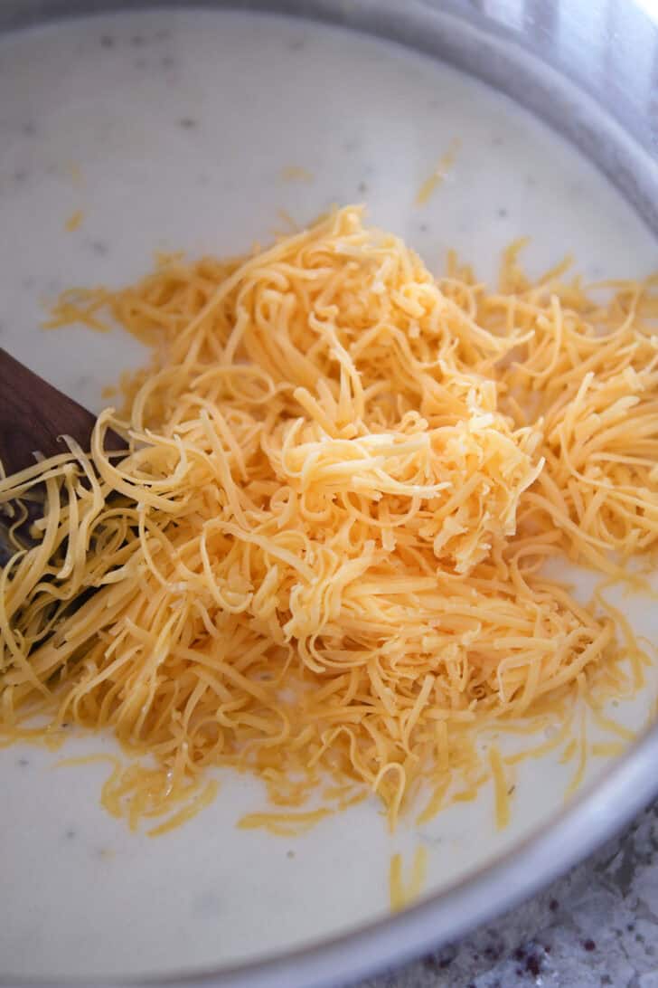 Top down view of a white sauce in a pot with shredded cheddar cheese on top.