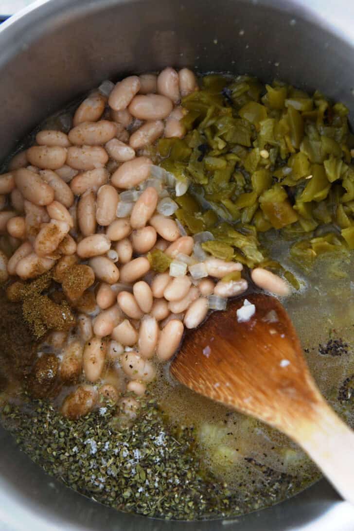 Top down view of an instant pot full of white beans, broth, seasonings, and diced chiles.