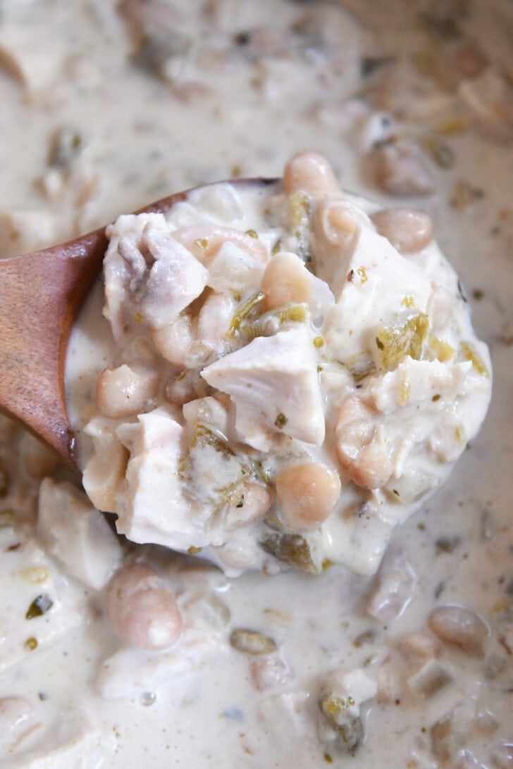 Top down view of a wooden ladle full of creamy white chicken chili.