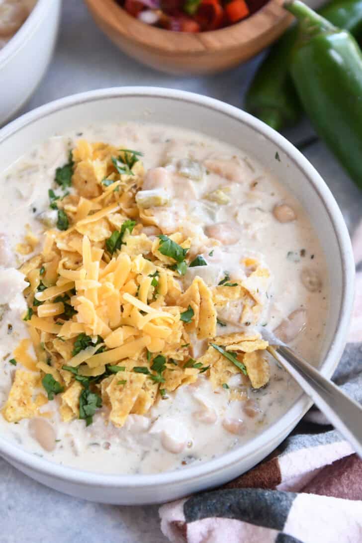 Top down view of a white bowl of white chicken chili topped with shredded cheddar cheese, chopped cilantro, and crushed tortilla chips.