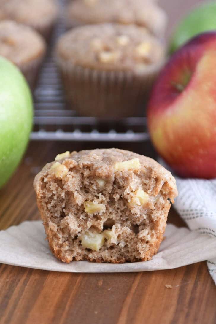 Half of apple cinnamon muffin with apple pieces on paper liner.