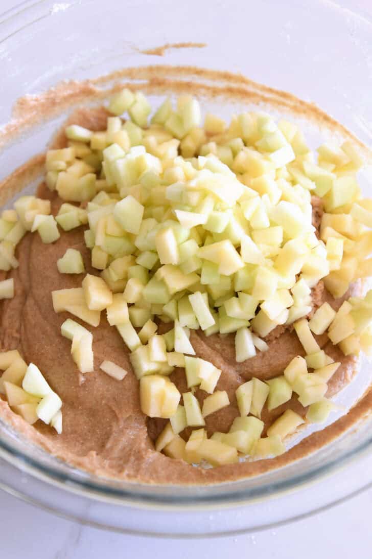 Fresh apple pieces on top of muffin batter in glass bowl.