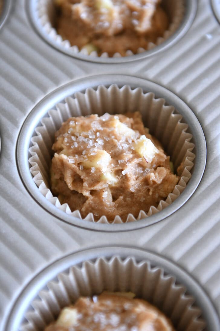 Unbaked apple muffin batter in paper liner in muffin tin.