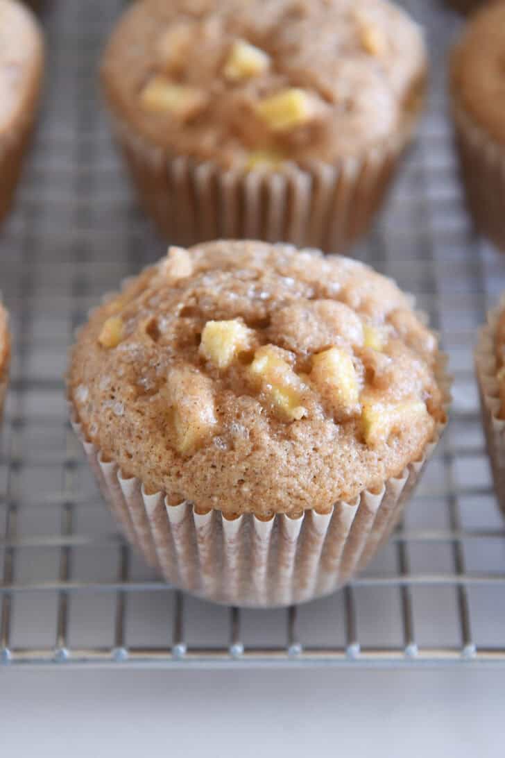 Baked apple cinnamon muffin in paper liner on cooling rack.