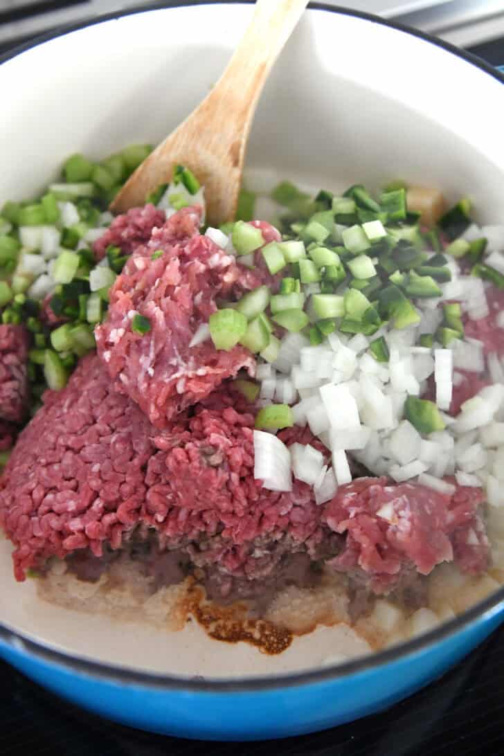 Cast iron pot with ground beef, ground pork, jalapenos, bell peppers, onions and garlic.