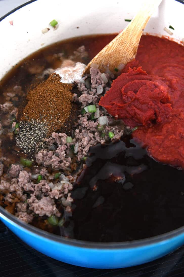 Cast iron pot with ground beef, tomato paste, crushed tomatoes, BBQ sauce, chili powder, and salt.
