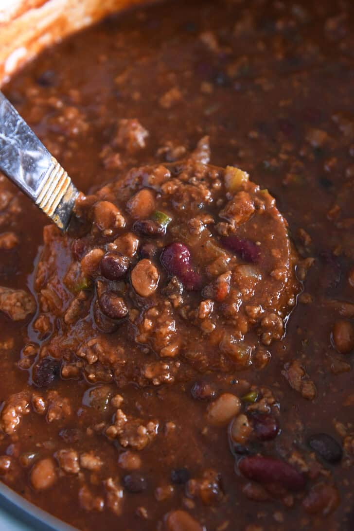 Ladle scooping beef and bean chili in cast iron pot.