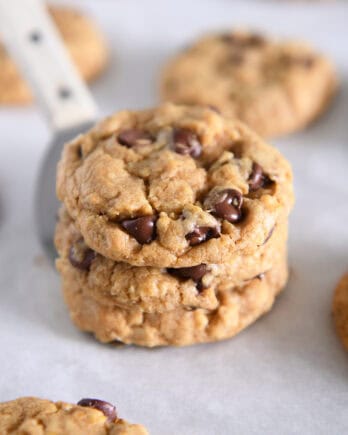 Three pumpkin oatmeal chocolate chip cookies stacked on a spatula.